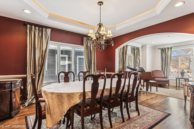 dining room with an inviting chandelier, a tray ceiling, arched walkways, and dark wood-type flooring