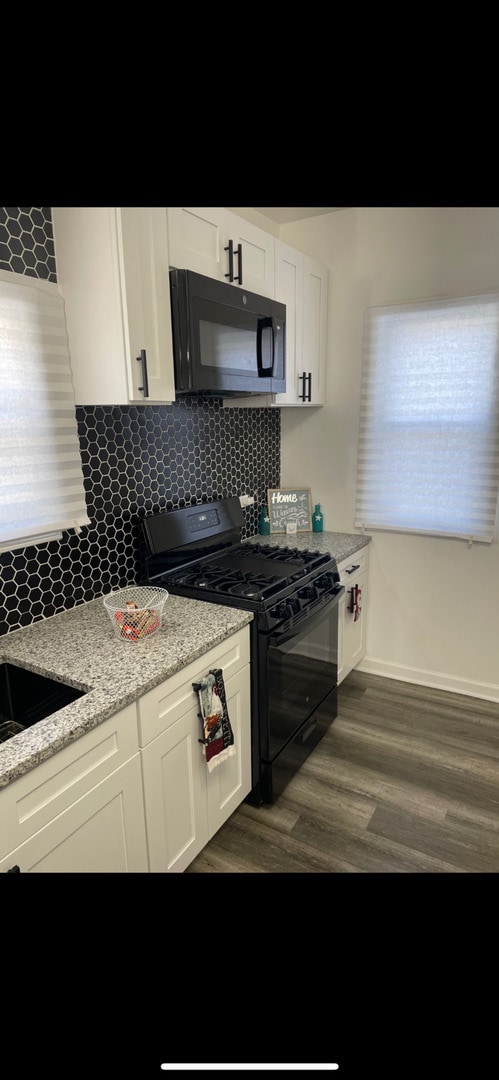 kitchen with white cabinetry, light stone countertops, black appliances, and dark hardwood / wood-style flooring