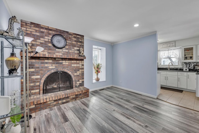 unfurnished living room featuring ornamental molding, a brick fireplace, a sink, light wood-type flooring, and baseboards