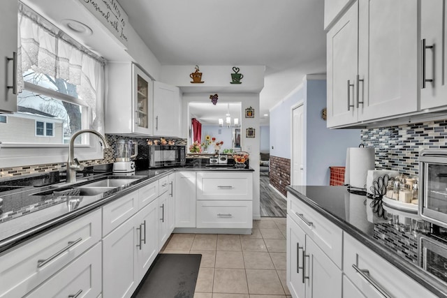 kitchen with light tile patterned floors, glass insert cabinets, white cabinets, a sink, and black microwave