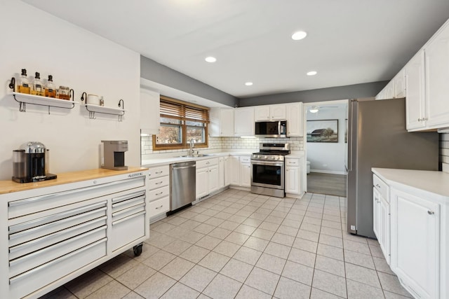 kitchen featuring tasteful backsplash, stainless steel appliances, light tile patterned flooring, sink, and white cabinetry