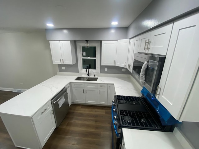 kitchen with kitchen peninsula, sink, light stone counters, appliances with stainless steel finishes, and white cabinets