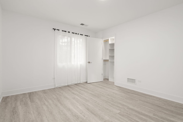 unfurnished bedroom featuring light wood-type flooring, a walk in closet, and a closet