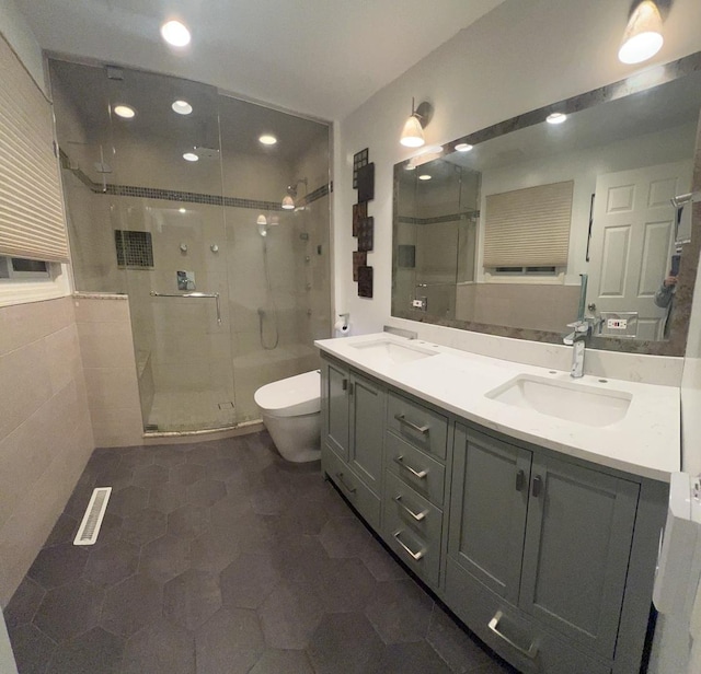 full bath featuring toilet, a stall shower, double vanity, and a sink