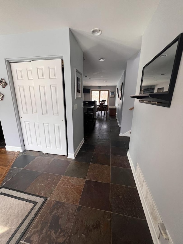 hall with stone tile floors and baseboards