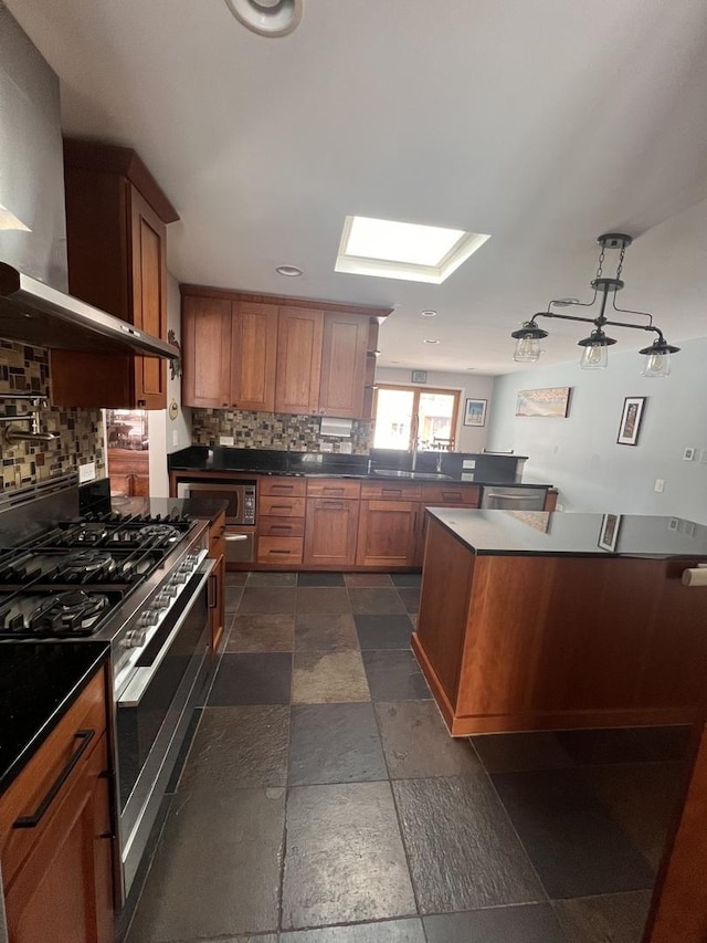 kitchen with stone tile floors, brown cabinetry, appliances with stainless steel finishes, wall chimney range hood, and backsplash