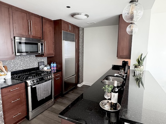 kitchen with dark wood-style flooring, a sink, appliances with stainless steel finishes, tasteful backsplash, and dark stone countertops