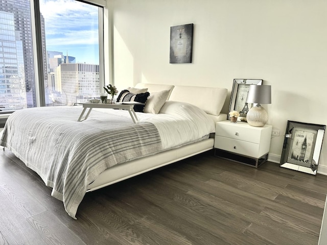 bedroom with dark wood-style floors, baseboards, and a city view