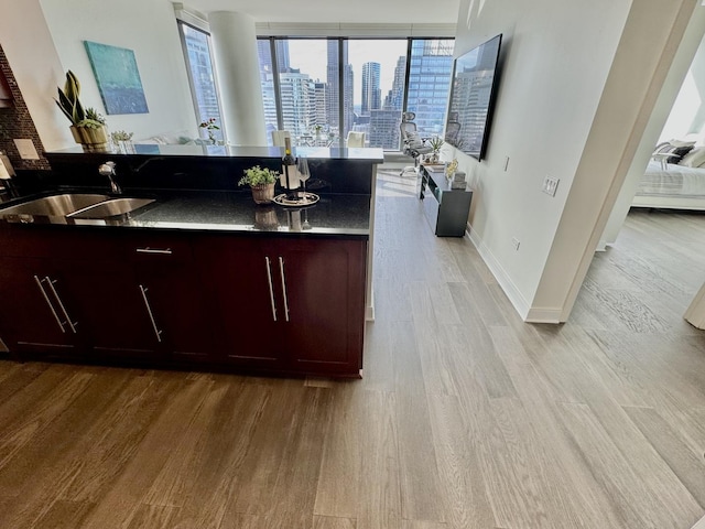 kitchen featuring light wood finished floors, baseboards, dark countertops, open floor plan, and a sink