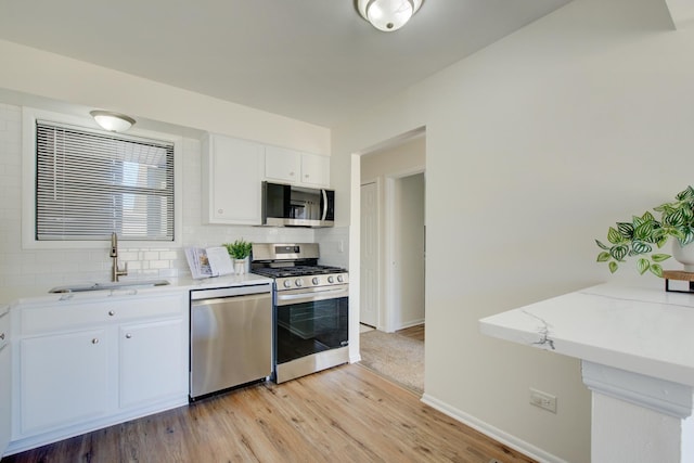 kitchen featuring a sink, white cabinetry, light wood-style floors, appliances with stainless steel finishes, and tasteful backsplash