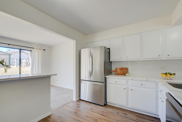 kitchen featuring stainless steel appliances, white cabinets, light wood-style floors, and backsplash