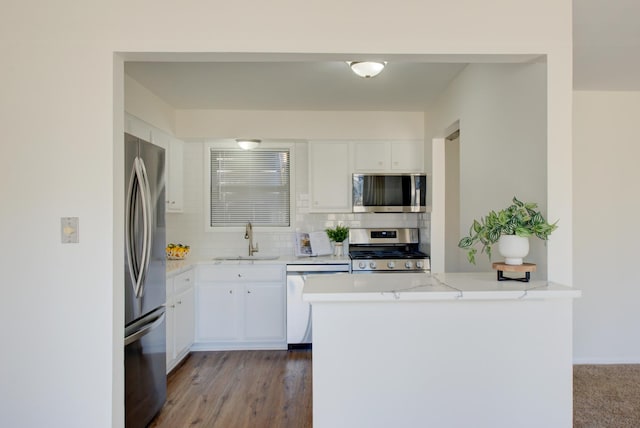 kitchen with decorative backsplash, appliances with stainless steel finishes, white cabinetry, a sink, and a peninsula