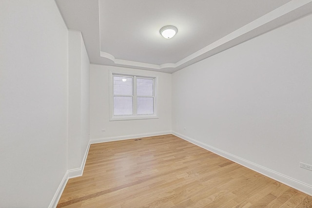 spare room featuring light wood-type flooring, a raised ceiling, and baseboards