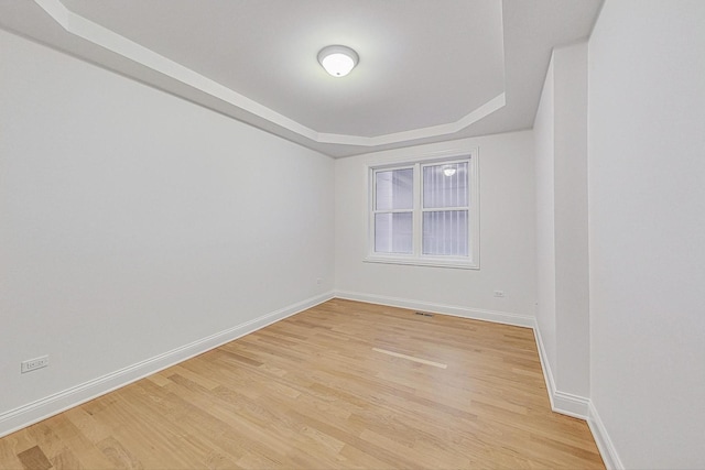 unfurnished room with light wood finished floors, a tray ceiling, and baseboards