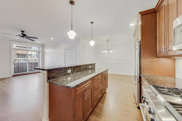 kitchen featuring brown cabinetry, light wood-style flooring, a kitchen island, dark stone countertops, and stainless steel appliances