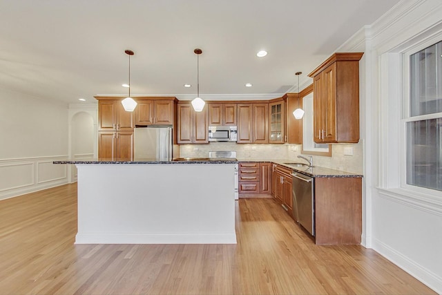 kitchen with brown cabinetry, light wood-style flooring, appliances with stainless steel finishes, dark stone countertops, and a sink