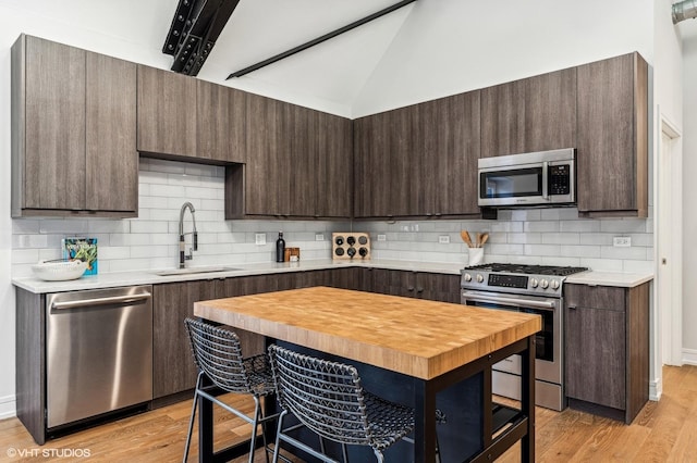 kitchen featuring appliances with stainless steel finishes, sink, light hardwood / wood-style flooring, and lofted ceiling