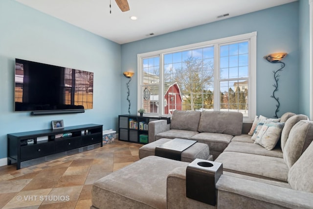 living room with a ceiling fan, a wealth of natural light, stone finish flooring, and visible vents