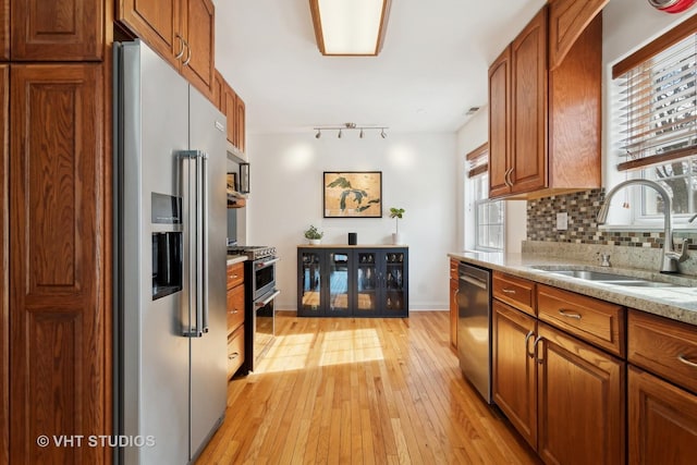 kitchen featuring stainless steel appliances, a sink, light wood-type flooring, decorative backsplash, and brown cabinets