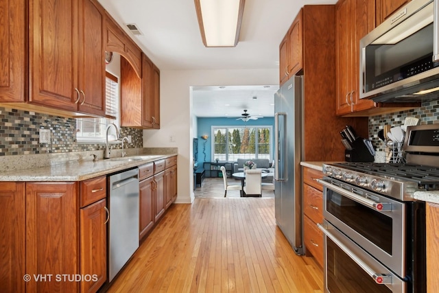 kitchen featuring stainless steel appliances, a sink, visible vents, light stone countertops, and brown cabinetry