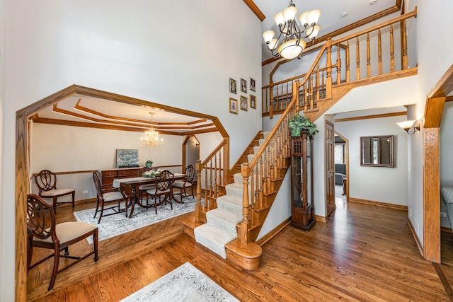 staircase with crown molding, a towering ceiling, a chandelier, and wood-type flooring