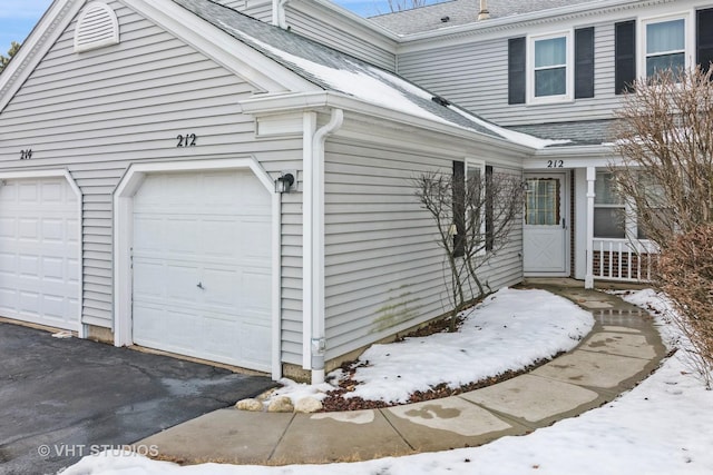 view of snowy exterior featuring a garage and a shingled roof