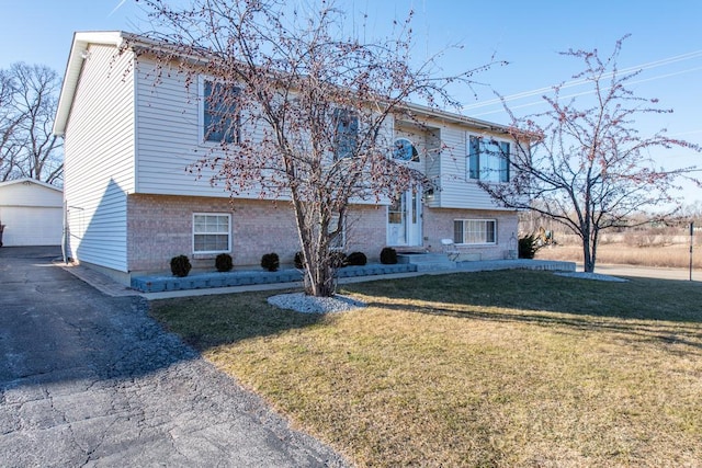 bi-level home with a garage, brick siding, a front yard, and an outdoor structure