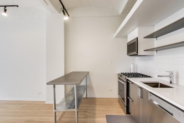 kitchen featuring light wood finished floors, tasteful backsplash, stainless steel appliances, open shelves, and a sink