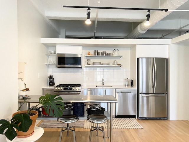 kitchen featuring light wood-style flooring, appliances with stainless steel finishes, open shelves, and decorative backsplash