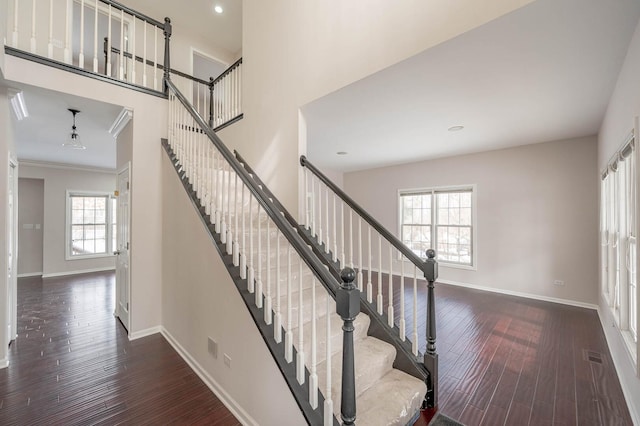 staircase featuring crown molding, a towering ceiling, baseboards, and wood finished floors