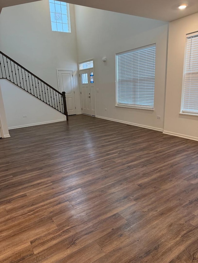 unfurnished living room featuring dark wood-type flooring and a towering ceiling