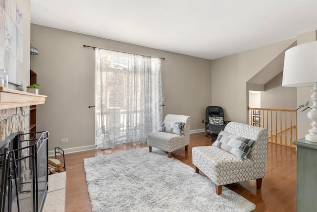 living area featuring baseboards, a stone fireplace, an upstairs landing, and wood finished floors