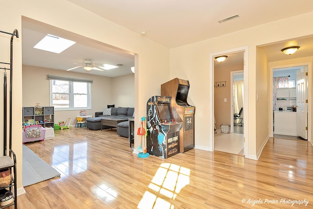 interior space with light wood finished floors, a skylight, visible vents, baseboards, and ceiling fan