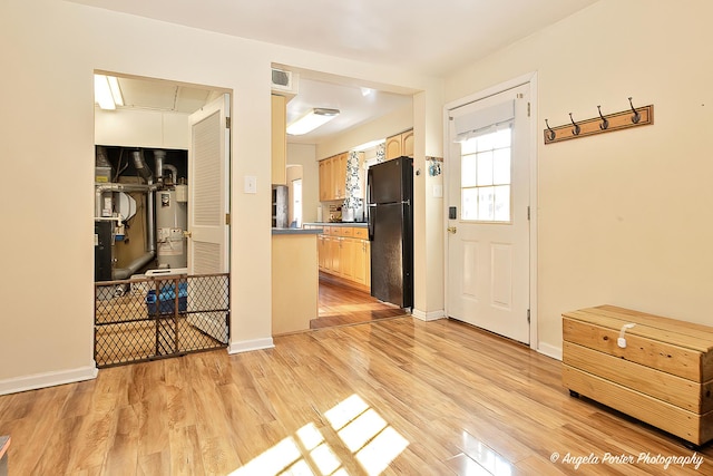 interior space featuring gas water heater, light wood-style floors, freestanding refrigerator, light brown cabinets, and baseboards