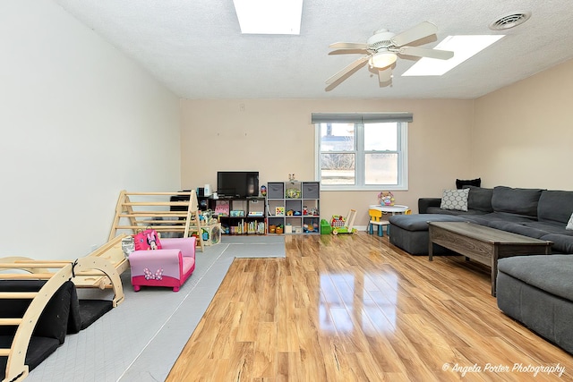 rec room with a ceiling fan, visible vents, light wood-style flooring, and a textured ceiling