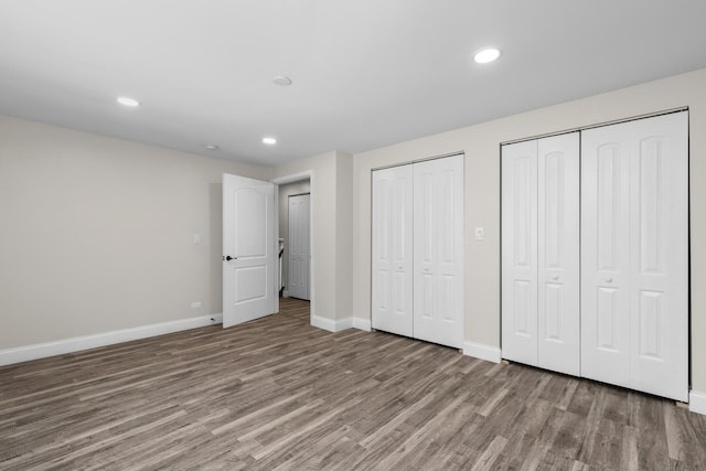 unfurnished bedroom featuring hardwood / wood-style floors and two closets