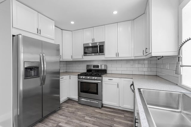 kitchen featuring stainless steel appliances, sink, tasteful backsplash, wood-type flooring, and white cabinets