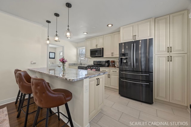 kitchen featuring light stone counters, cream cabinets, stainless steel appliances, a peninsula, and a kitchen breakfast bar