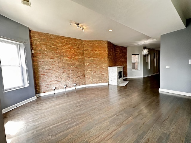 unfurnished living room with dark wood-type flooring, a brick fireplace, a notable chandelier, and brick wall