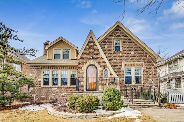 english style home with a shingled roof, a chimney, and brick siding