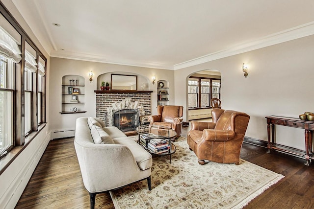 living room featuring built in shelves, a brick fireplace, a baseboard heating unit, and dark wood-style flooring