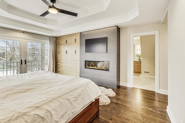 bedroom featuring a tile fireplace, dark wood-type flooring, access to outside, a raised ceiling, and crown molding