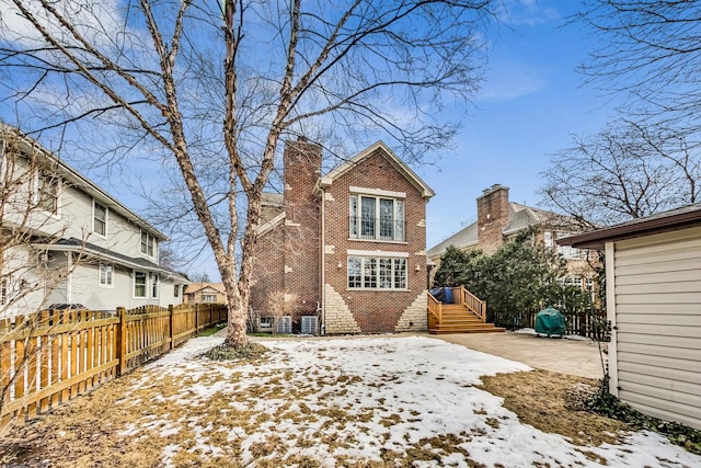 snow covered house with a chimney, fence, and brick siding