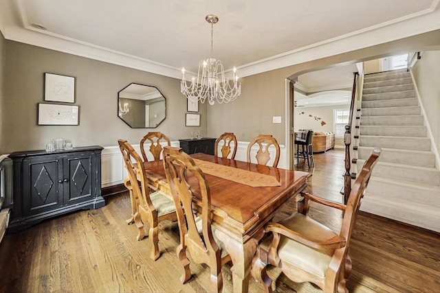 dining room featuring crown molding, stairs, arched walkways, and wood finished floors