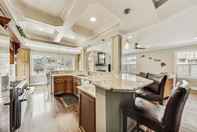 kitchen featuring a peninsula, a breakfast bar, hanging light fixtures, ornamental molding, and decorative columns