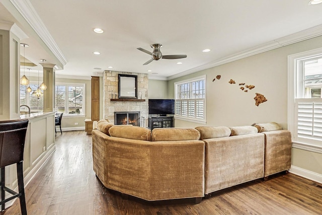 living area with baseboards, ornamental molding, wood finished floors, a fireplace, and ceiling fan with notable chandelier