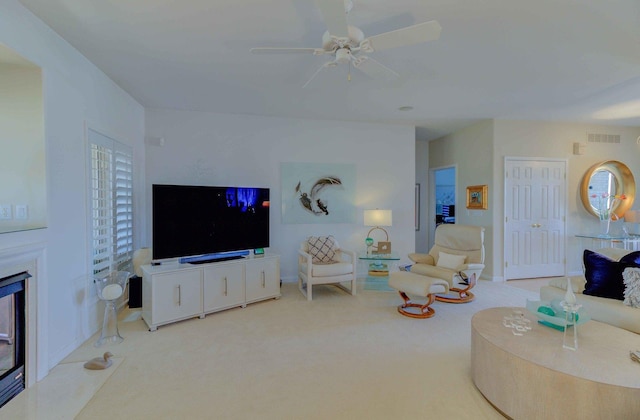 living room featuring ceiling fan, light colored carpet, visible vents, baseboards, and a glass covered fireplace