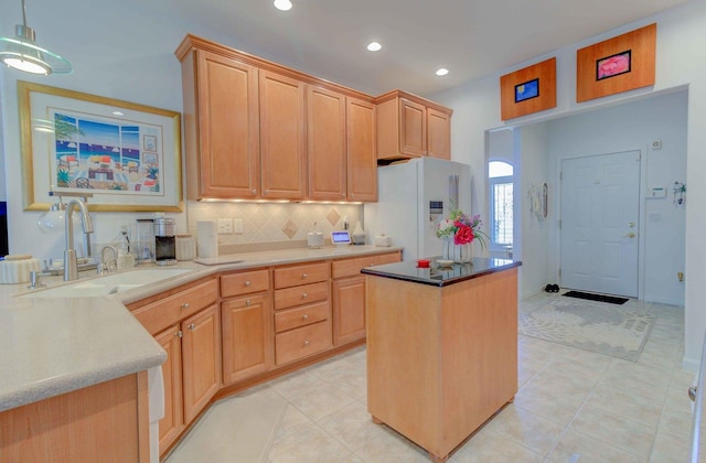 kitchen featuring white refrigerator with ice dispenser, a kitchen island, light countertops, light brown cabinets, and a sink