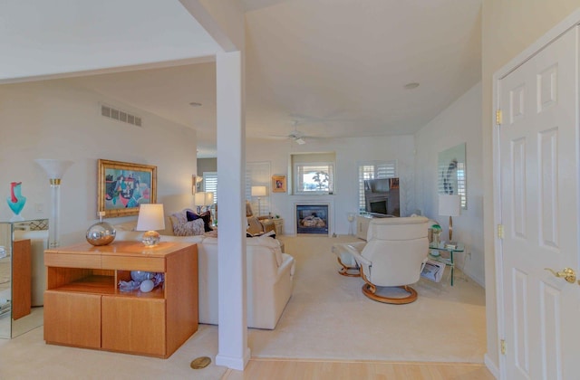 living room featuring a ceiling fan, a glass covered fireplace, and visible vents