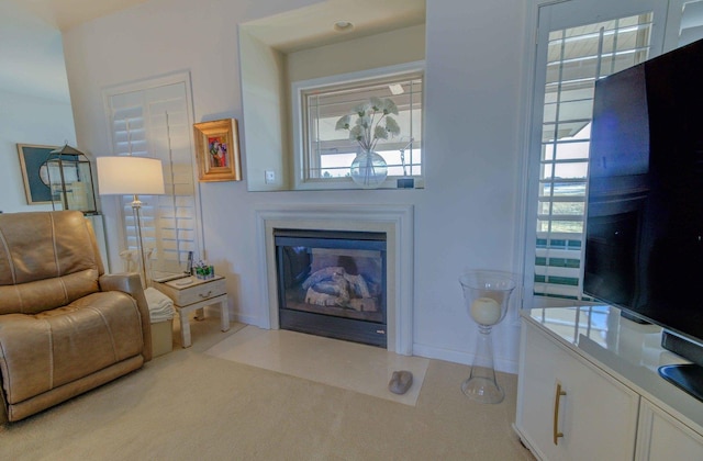 living room featuring light carpet, a fireplace with flush hearth, and baseboards